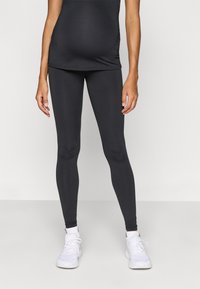 Μαύρα εγκυμοσύνης κολάν από ελαστικό ύφασμα, με εφαρμοστή σχεδίαση και ψηλή μέση για κάλυψη, συνδυασμένα με λευκά αθλητικά παπούτσια.