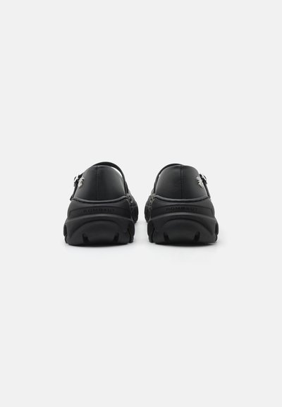 Sorte læder slip-on sko med kraftige teksturerede såler, der har en subtil logo detalje på hælen og et glat overdel design.