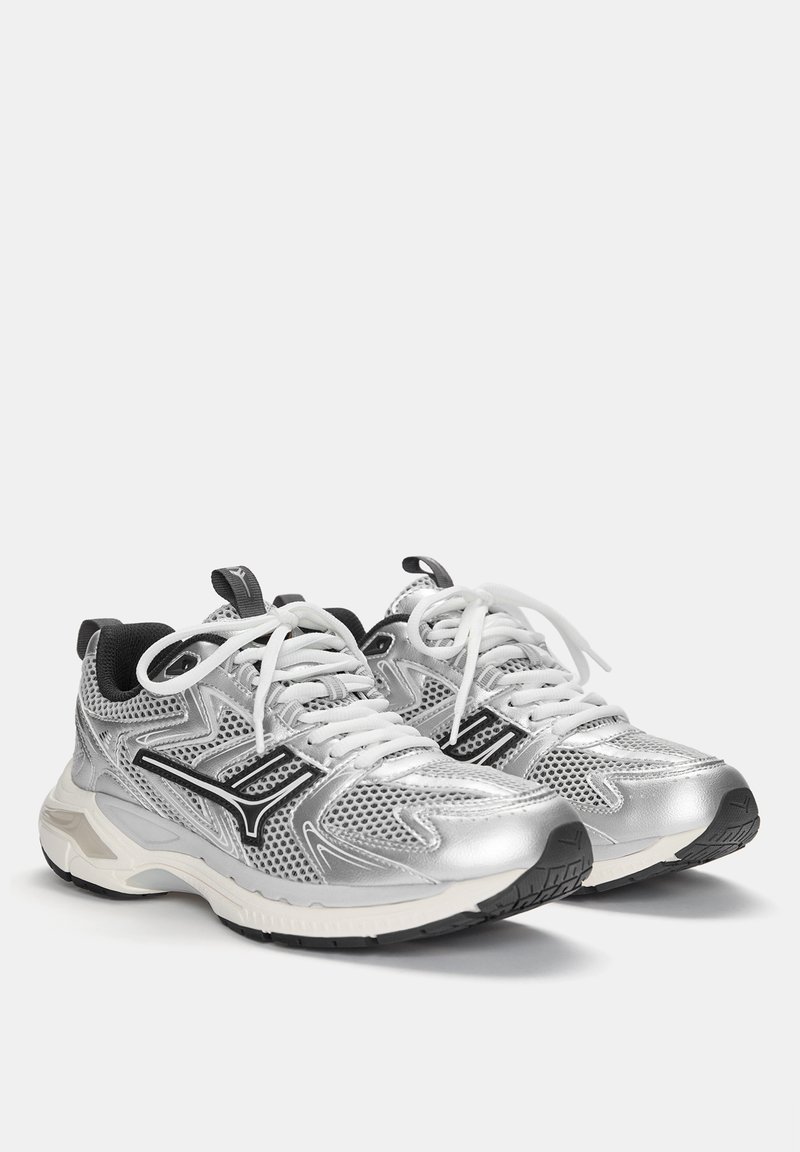 Baskets de sport argentées avec un dessus en mesh, accents noirs et lacets blancs. Avec une semelle rembourrée et un profil texturé pour l'adhérence.