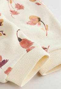 Tela de color crema con puños acanalados y un delicado patrón floral en tonos suaves de rosa, naranja y marrón.