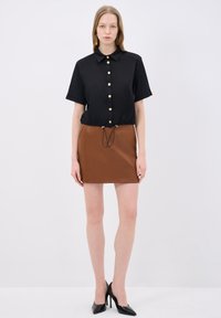 Camicia nera a maniche corte con bottoni dorati, cordoncino in vita, abbinata a una mini gonna in pelle marrone e tacchi alti neri.