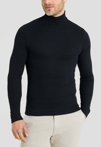Maglia a collo alto nera realizzata in un tessuto liscio e elasticizzato. Maniche lunghe e design aderente, con colletto alto e senza motivi visibili.