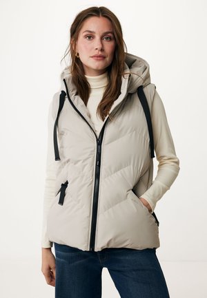 Beige padded vest with a hood, zip front, and black hardware details. Textured panels and adjustable ties on shoulders. Worn over a cream top.