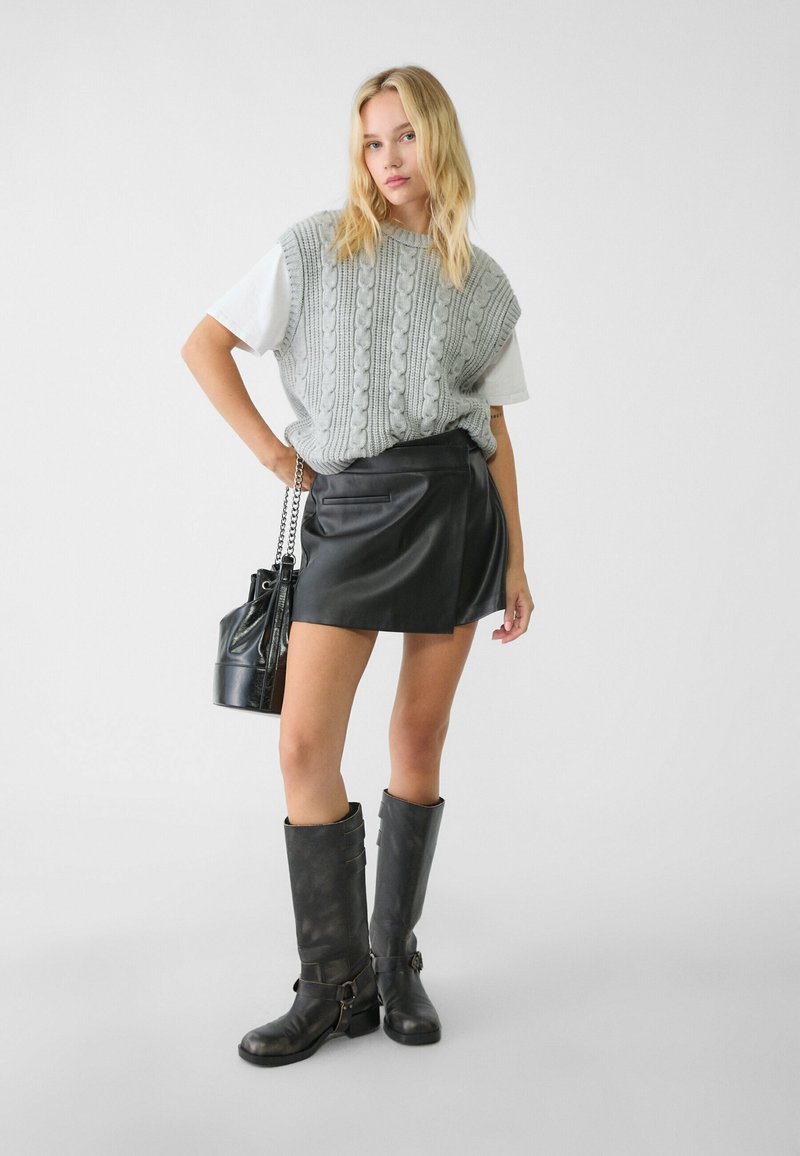 Maglione grigio lavorato a maglia oversize abbinato a una mini gonna in pelle nera, stivali neri al ginocchio e una piccola borsa a spalla nera.
