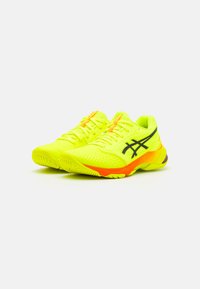 Scarpe da ginnastica neon gialle con un design testurizzato, logo nero e accenti arancioni sulla suola e sui lacci. Leggere e traspiranti.