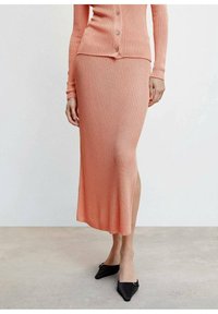 Ensemble en tricot côtelé à deux pièces en corail, comprenant un cardigan à boutons et une jupe crayon midi avec une fente latérale, accompagnés de ballerines noires à bout pointu.