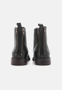 Stivaletti neri in pelle con doppie cerniere argentate, punta tondeggiante e tacco impilato. Tessuto liscio con un design minimalista.