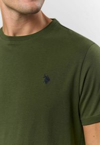 Olivgrön t-shirt av mjukt material med rund halsringning och korta ärmar. Logotyp i mörkblått broderad detalj.