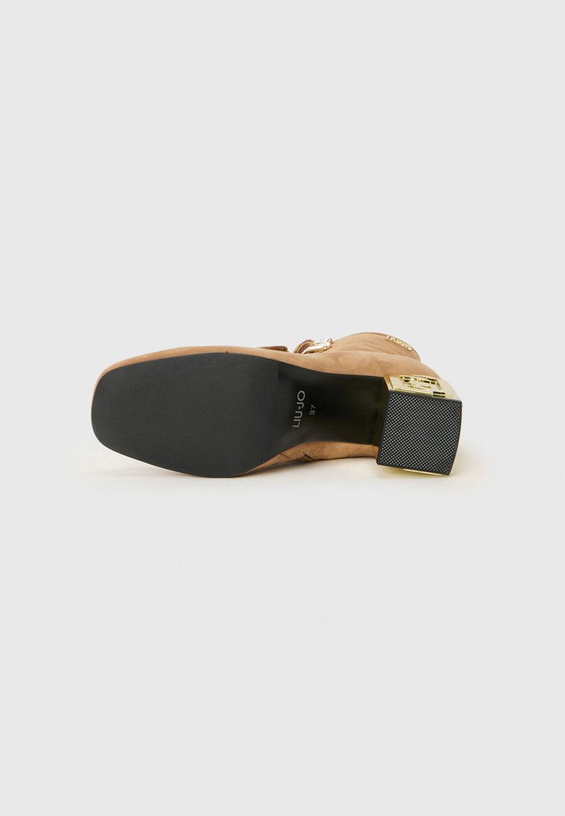 Beiger Wildleder-Ankle-Boot mit goldfarbenen Beschlägen, Blockabsatz und strukturiertem schwarzen Sohlen. Verfügt über einen seitlichen Reißverschluss und ein rundes Zehendesign.