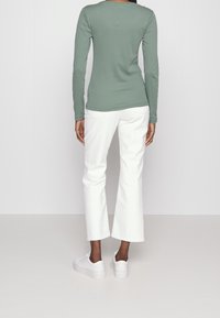 Pitkähihaista vihreää paitaa yhdistetty valkoisiin leveisiin housuihin ja valkoisiin lenkkareihin. Asu korostaa rentoa, mukavaa tyyliä.