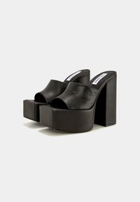 Mules à plateforme noires à talons hauts épais, bout ouvert et design facile à enfiler sur un fond clair uni.