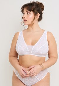 Bralette in pizzo bianco con motivi floreali, design a V profonda, spalline larghe e sotto-petto morbido. Abbinato a culotte in pizzo coordinate.