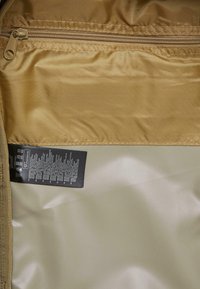 Gold fabric interior of a bag featuring a smooth texture, a zippered pocket, and a care label with washing instructions attached.