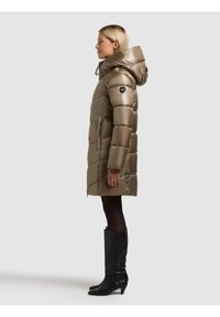 Pufferjacka i metallisk brons, knälång med huva, med quiltad design och sidfickor. Kombinerad med knähöga svarta stövlar.