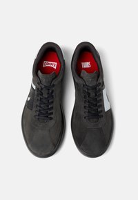 Gray suede sneakers with black laces, white accents, and red insoles. Minimalist design with a rounded toe and rubber sole.