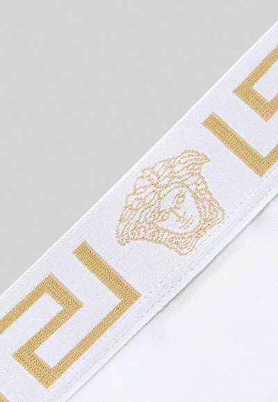 Tessuto bianco con logo Medusa dorato e motivo geometrico. Il nastro ha una texture liscia e presenta audaci accenti dorati a contrasto.