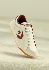 White leather sneaker with maroon accents, featuring a star logo, perforated toe, and a cream rubber sole. Laces are white.