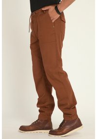 Pantalons cargo bruns avec taille à cordon, poignets élastiques, multiples poches et texture lisse, associés à des bottes brunes à lacets.