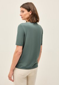 Mørkegrøn kortærmet T-shirt lavet af blødt bomuld, med rund halsudskæring og lige snit, vist fra ryggen.