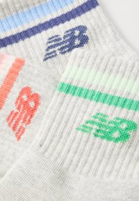 Tre par strømper med ribbet gråt stof, farvede striber og brandlogoer i blå, grøn og koral.
