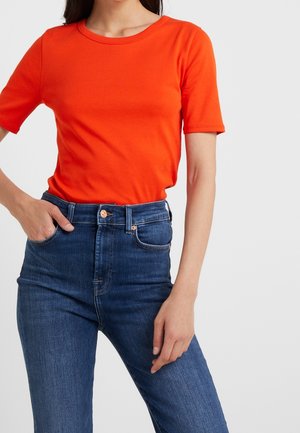 Kortærmet orange bomuld T-shirt kombineret med højtaljede mørkeblå denimjeans med lommer og knaplukning.