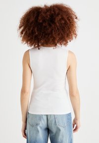White sleeveless top with a fitted design, ribbed texture, and round neckline, paired with light blue high-waisted jeans.