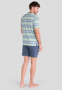 Camiseta de manga corta a rayas en azul, verde y gris con cuello redondo y cortes laterales, combinada con pantalones cortos azules, modelo de pie descalzo.