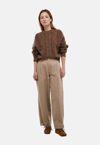 Pull en maille brun avec un motif texturé, associé à un pantalon large beige et des chaussures à lacets en daim marron.