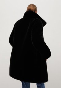 Czarny futerko z wysokim kołnierzem i luźnym krojem. Miękka tekstura i gładkie wykończenie. Widok z tyłu, zestawione z niebieskimi dżinsami.