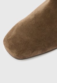 Bottine en daim marron avec une semelle plate, un bout carré et une texture lisse ; sans quincaillerie ni motifs visibles.