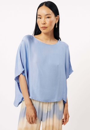 Haut en soie bleu clair avec un large col bateau, des manches amples et une forme évasée. Texture lisse avec un éclat subtil, associé à un pantalon à motifs.