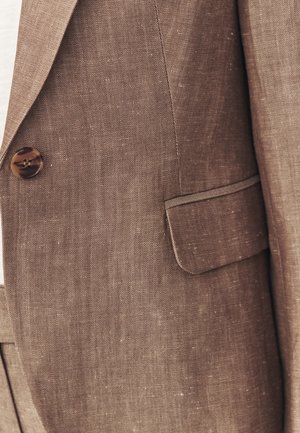 Nahaufnahme eines braunen, strukturierten Blazers mit Knopf und Klappentasche an der linken Seite.