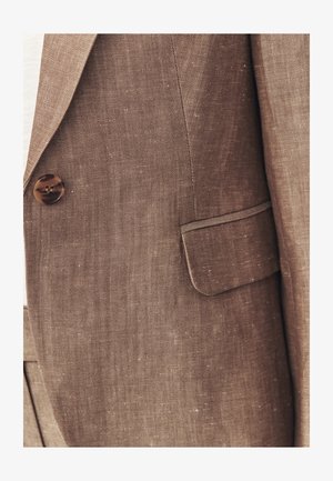 Close-up of brown textured blazer with button and flap pocket detail on left side.