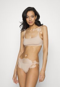 Beige stretch stof crop top en bikini set met dunne bandjes. Kenmerkt een huidkleurmatching kleur en een gladde textuur. Huid met lichte patronen.