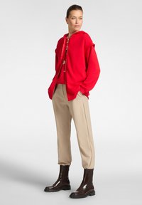 Sudadera roja con cremallera frontal, pantalones beiges holgados y botas cortas marrones. Tejido suave, corte relajado, diseño minimalista.