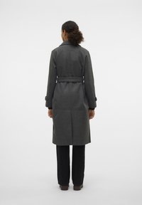 Grå ullfrakk, midt på leggen, med belte i midjen, notched krage og knappede mansjett detaljer. Glatt tekstur, minimalistisk design.