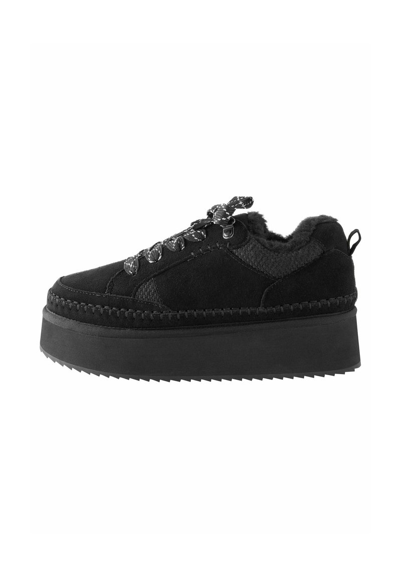 Zapatilla plataforma negra con parte superior texturizada, forro de piel de pelo y cordones decorativos. Presenta una gruesa suela de goma estriada y detalles cosidos.