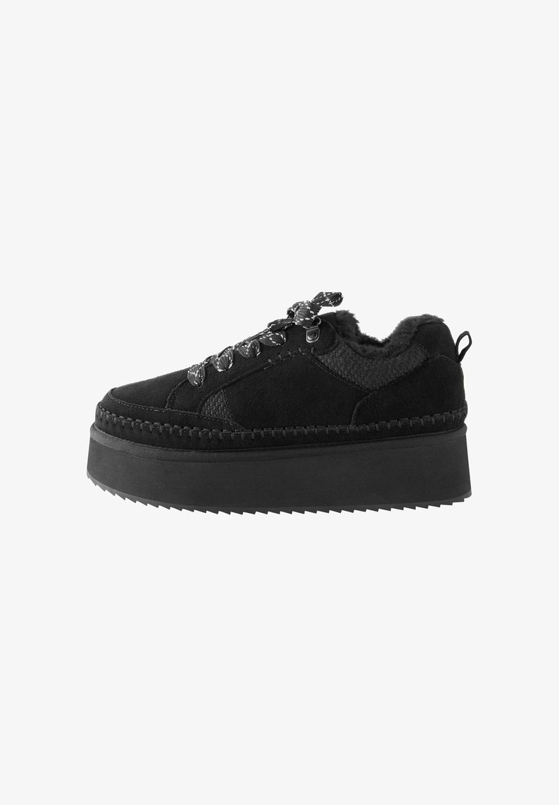 Black platform sneaker with a textured upper, fur lining, and decorative laces. Features a thick, ridged rubber sole and stitched details.