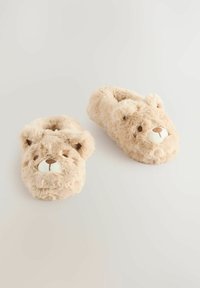 Des chaussons en peluche beige flou en forme d'ours, avec un bout arrondi, des détails faciaux cousus et une fourrure douce et texturée.