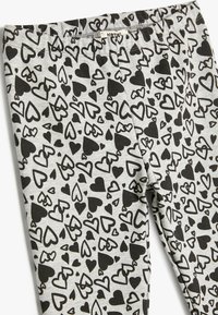 Bomuldsleggings med en grå baggrund og et mønster af sorte hjerter. Taljen er elastisk, og stoffet virker blødt og struktureret.