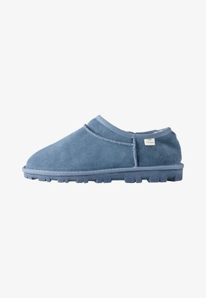Weicher blauer Slipper mit strukturierter Sohle und kleinem Stoffetikett an der Oberseite, von links im Profil vor weißem Hintergrund gezeigt.