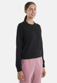 Sudadera negra con cuello redondo y puños acanalados, con un corte holgado. Combinada con pantalones sueltos de color rosa claro. Textura suave.