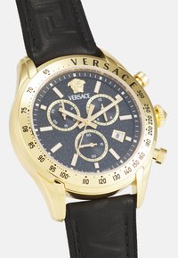 Orologio cronografo Versace dorato con quadrante текстurato nero, cinturino in pelle nera e dettagli dorati; presenta tre sottoquadranti e finestra per la data.