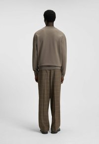 Felpa grigia con colletto rotondo e spalle cadenti, abbinata a pantaloni a quadri marroni. L'outfit presenta una vestibilità rilassata e tessuti morbidi.