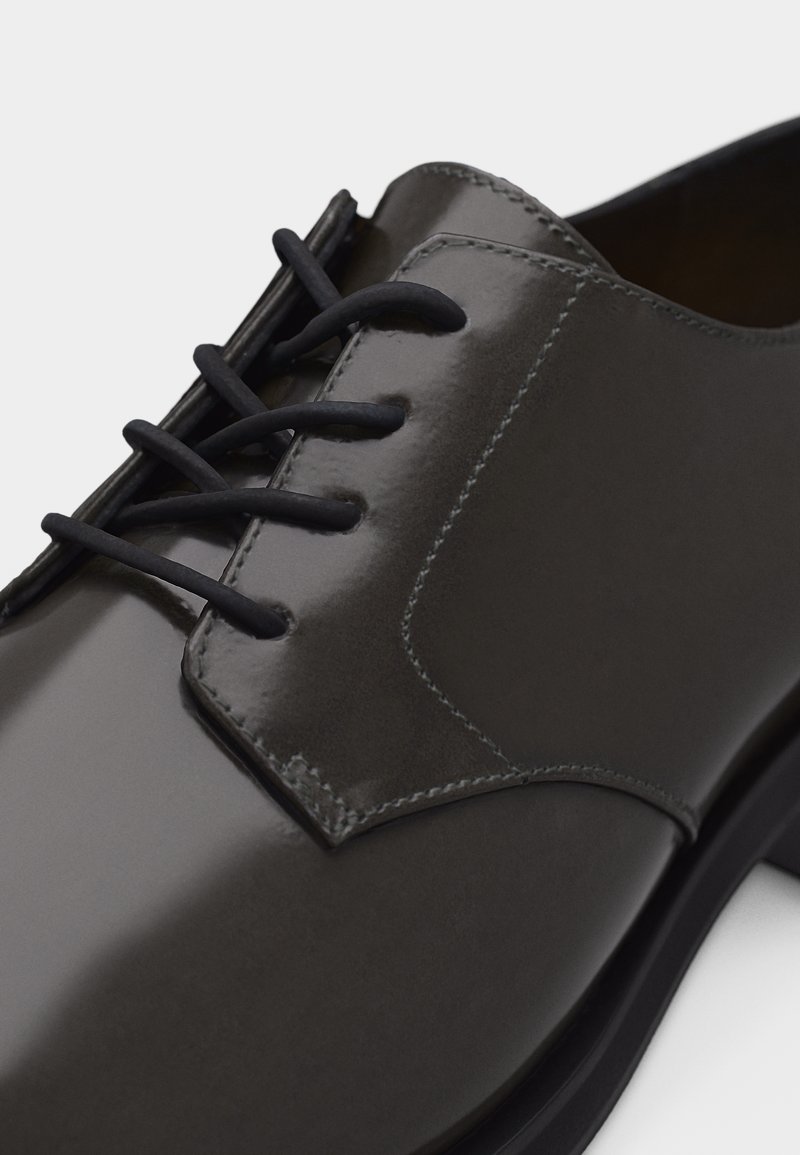 Black polished leather dress shoe with black laces and detailed stitching on the vamp and quarters, shown in close-up.