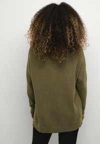 Olivgrüner, gerippter Strickpullover mit langen Ärmeln, lockerer Passform, seitlichen Schlitzen und strukturiertem Oberflächen, von hinten betrachtet.