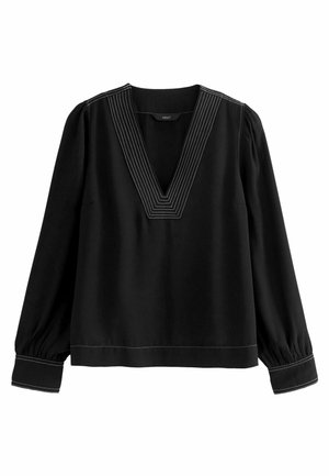 Blouse noire à manches longues avec un col en V profond, coutures contrastantes blanches le long de l'encolure, des poignets et de l'ourlet, et manches légèrement bouffantes avec poignets froncés.