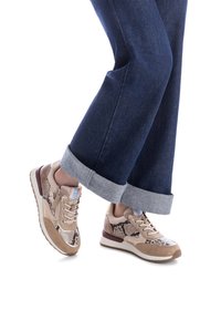 Zapatillas beige con patrones de piel de serpiente, acentos de ante y lengüeta acolchada. Suela ligera y tacón en contraste en color burdeos. Combinadas con jeans oscuros.