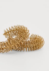 Goldene Metallcoil-Armbanduhr mit einem Spiraldesign aus sich überlappenden Schlaufen und einer glatten Oberfläche, die das Licht mit ihrer reflektierenden Oberfläche einfängt.