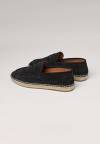 Mocasines de ante negro con suela de yute estilo espadrille, que presentan una costura elevada y diseño sin cierres. Forro interior de cuero marrón.